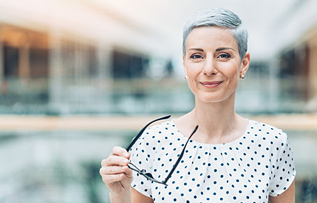 A mature woman holding a pair of eyeglasses.