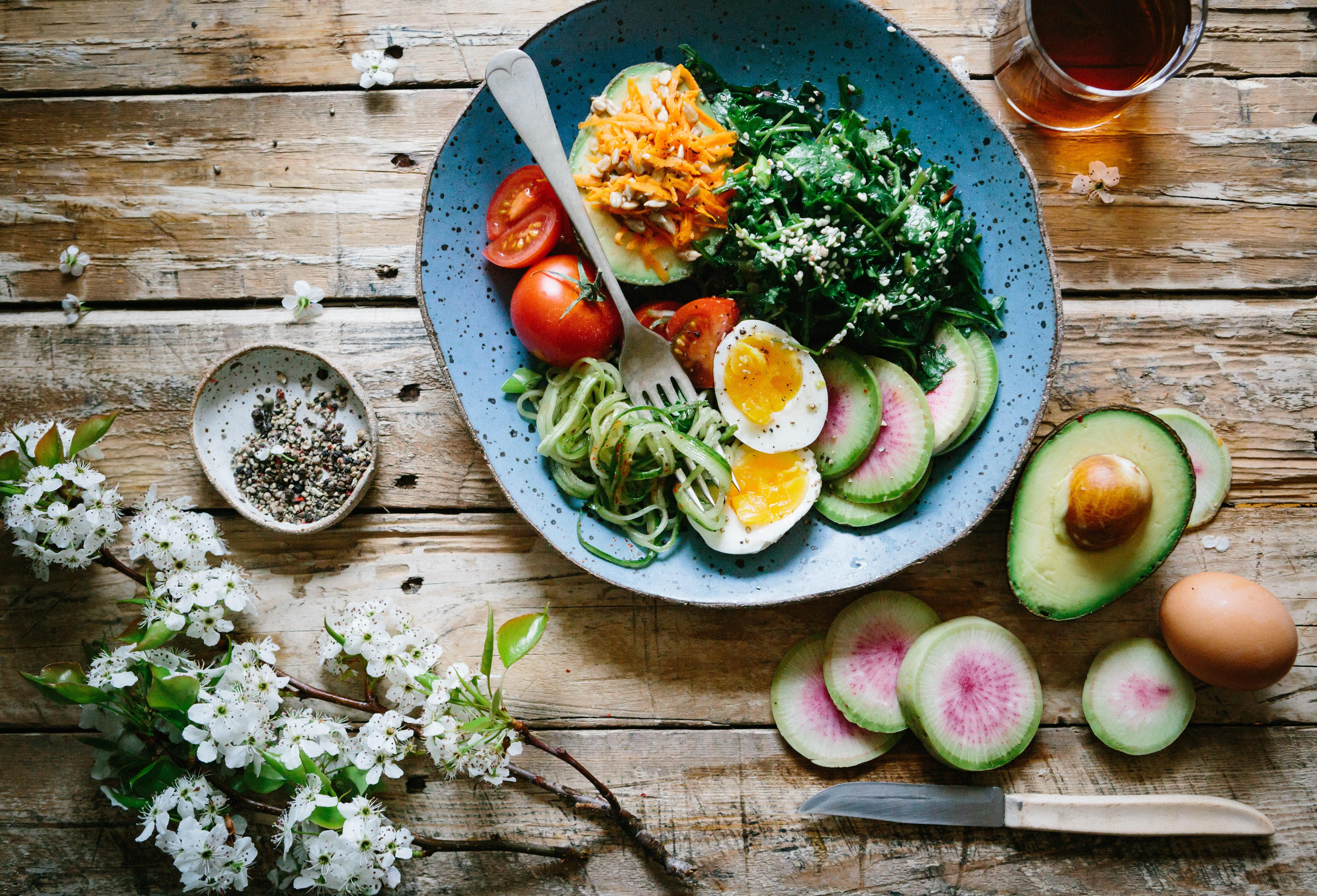 Bird's eye photo of a tasty looking lunch of eggs, salads, and avocado, alongside a cup of tea and some flowers.