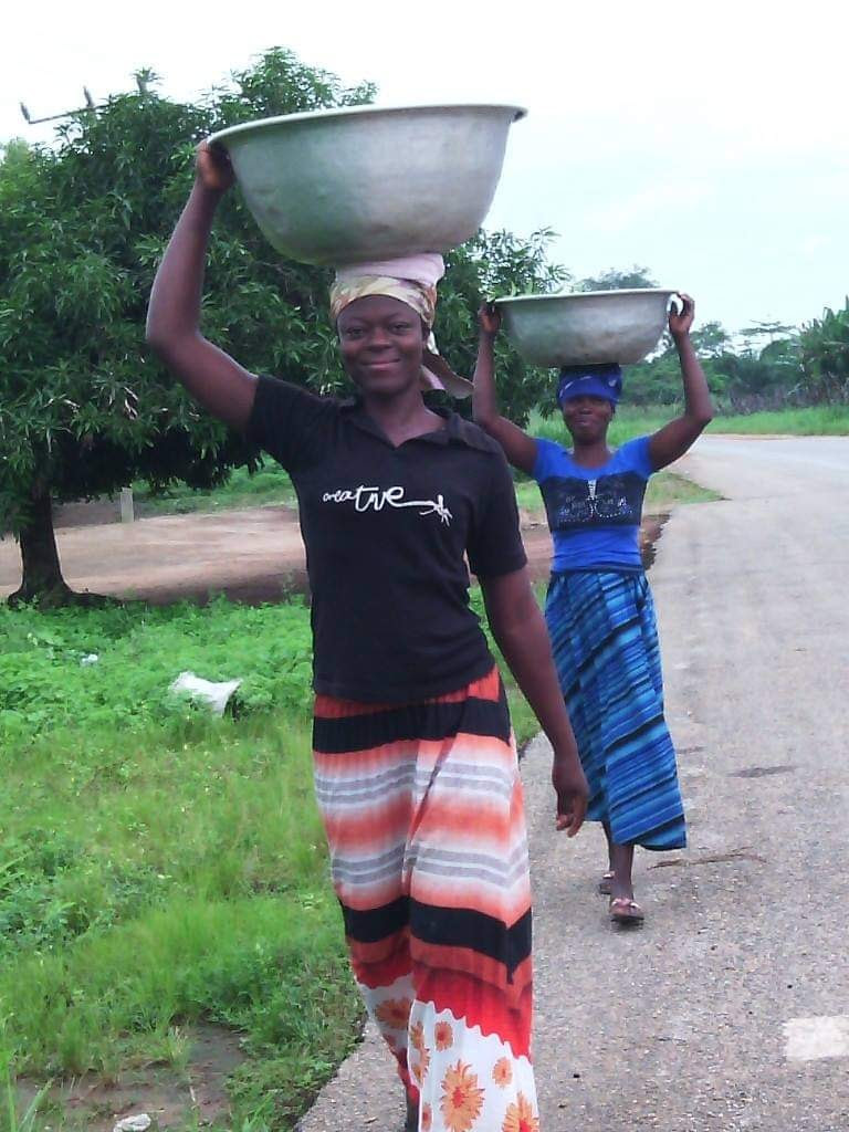 Two smiling women in Zambia carrying large pots on their heads.