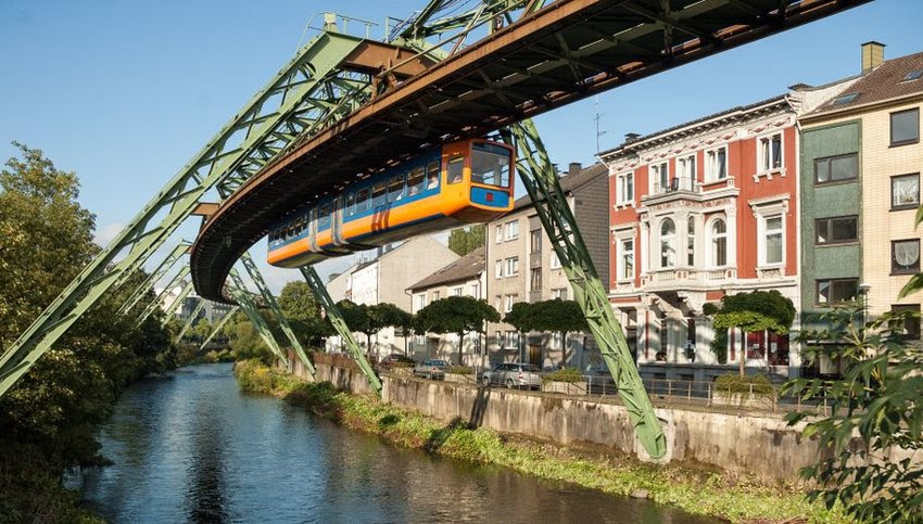 Orange and blue monorail suspended from tracks with houses lining the street below