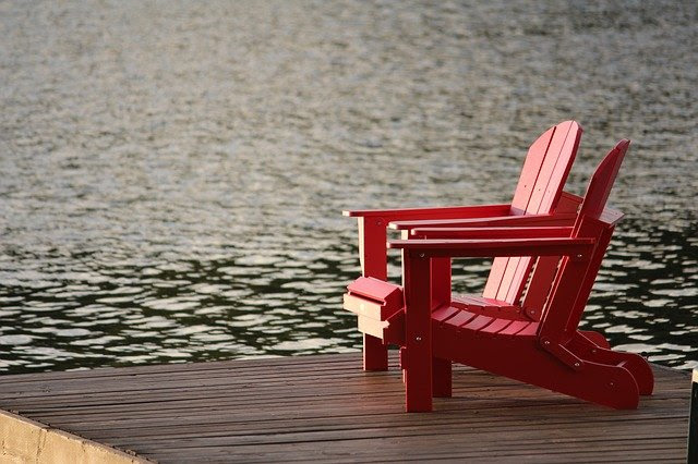 Photo of two red adirondack charis on a wooden dock in a lake.