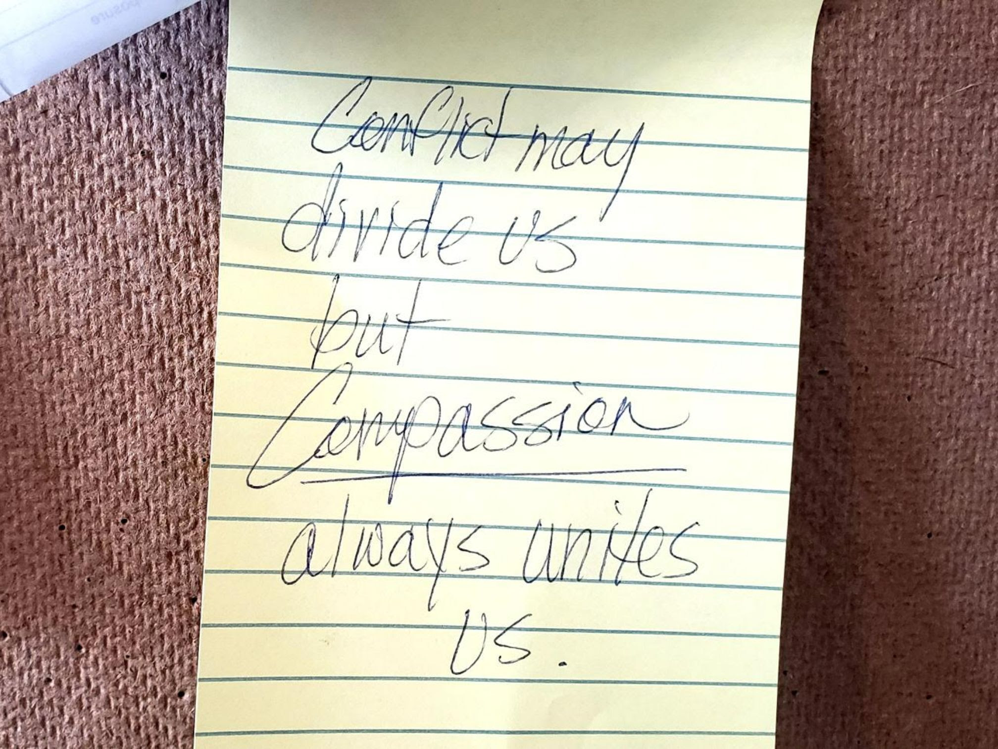 A post it note on a bulletin board reads, "Conflict may divide us but compassion always unites us."