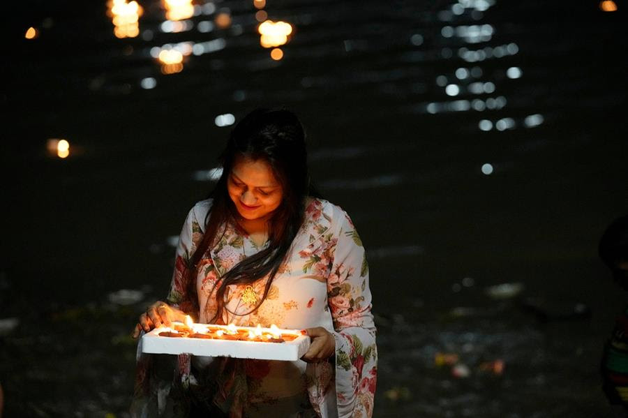 A Hindu woman lights oil lamps. The Hooghly River is visible in the background.