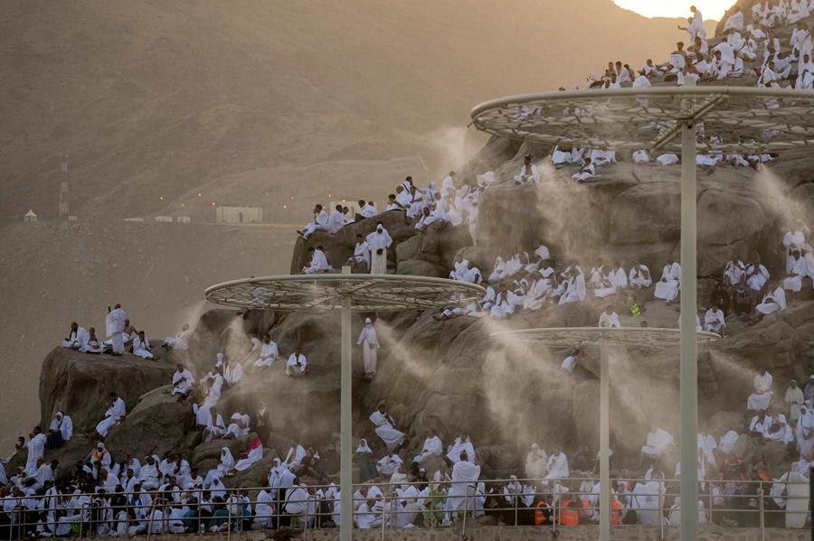 Muslim pilgrims pray on a rocky hill. There are fixtures that spray water mist.