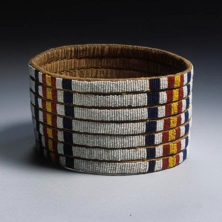 Luo headdress made from concentric layers of woven plant fibre, decorated with glass beads in white, dark blue, yellow and red.