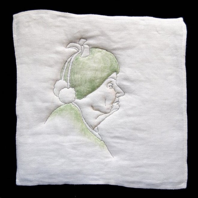 A white square of cloth on a black background with a stitched portrait of the head and shoulders of an older person in profile, wearing a green top and a round green hat with a bow and two pom poms dangling from it