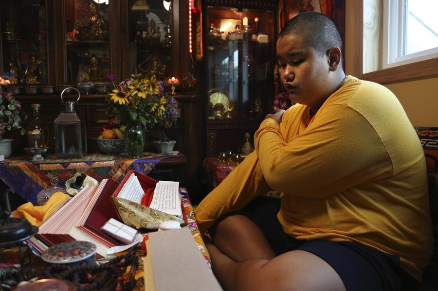 Jalue Dorje, 14, says his morning prayers. He is sitting cross legged with the prayers on the table in front of him.