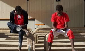 Adolescentes migrantes no acompañados leen panfletos informativos en Lampedusa (Italia) tras cruzar el Mediterráneo Central.