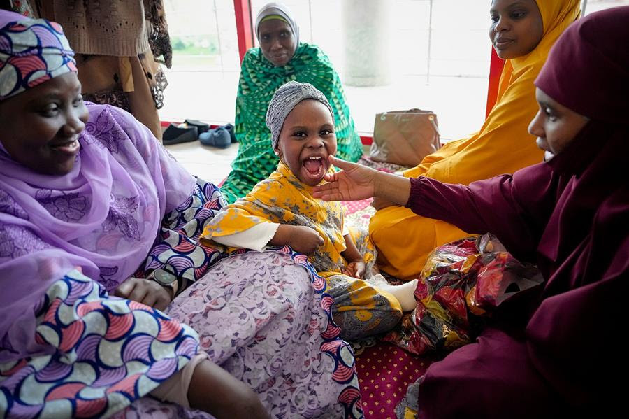 Women gather in the women's section before Eid al-Fitr prayers in Bucharest, Romania. A child sits in the center of the group laughing.