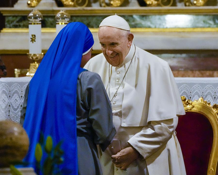 Pope Francis speaks with a nun wearing a blue habit.