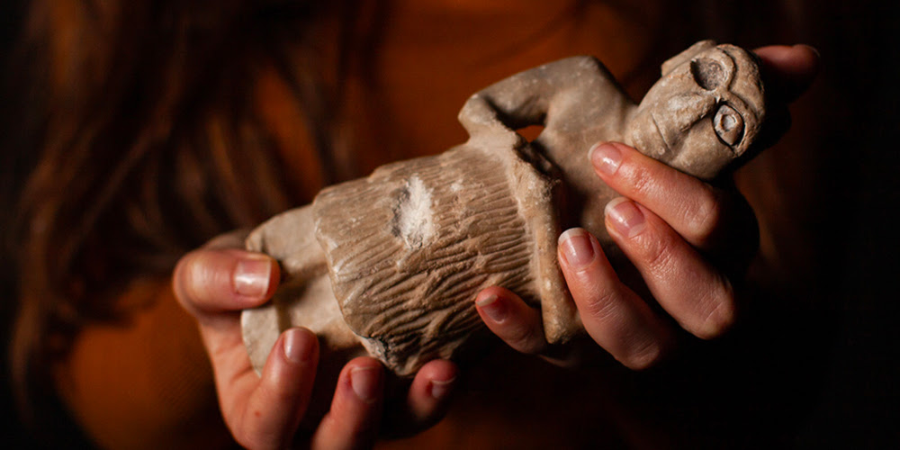 A pair of hands hold a Sumerian stone statue