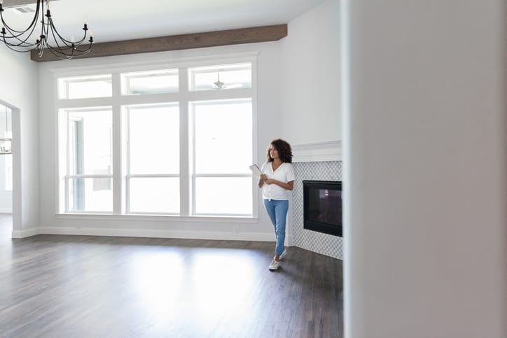 A woman walking through an empty family room with a clipboard in her hands.