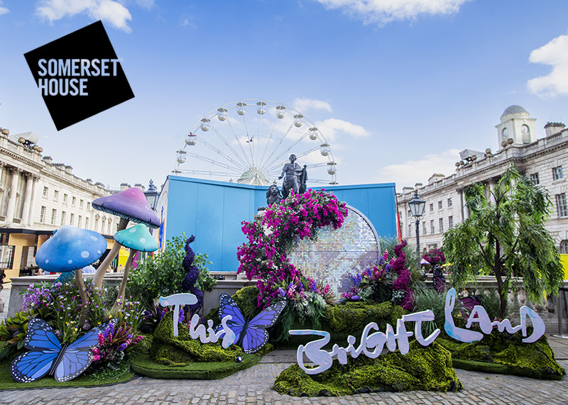 A photo of the entrance to This Bright Land at Somerset House. An installation of grassy mounds, house butterflies mushrooms and flowers. The words This Bright Land are placed artfully across the display.