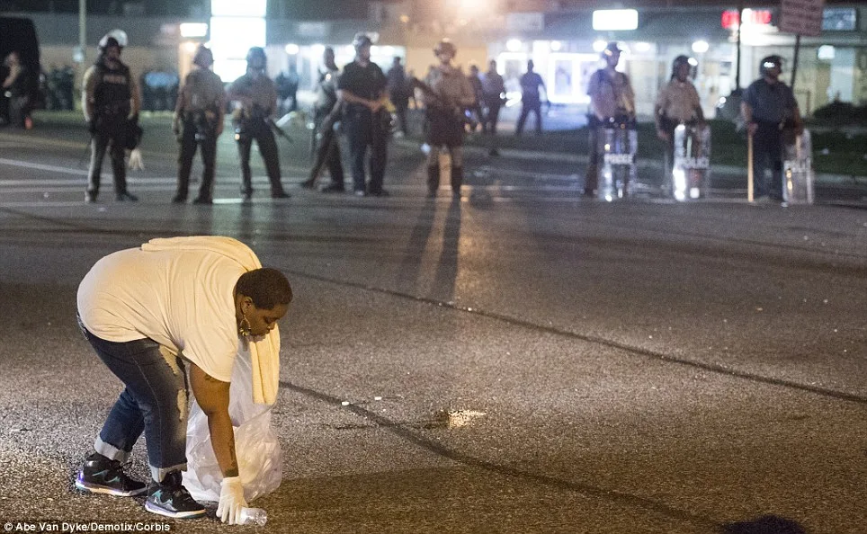 A woman picks up garbage in the street left over from protestors in Ferguson. Confrontation resumed as protestors marched towards heavily armed police on Monday night. Law enforcement reported 78 arrests