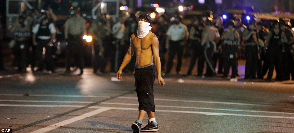 A lone man walks in front of heavily-armed police lines in Ferguson as 78 people are reported to have been arrested