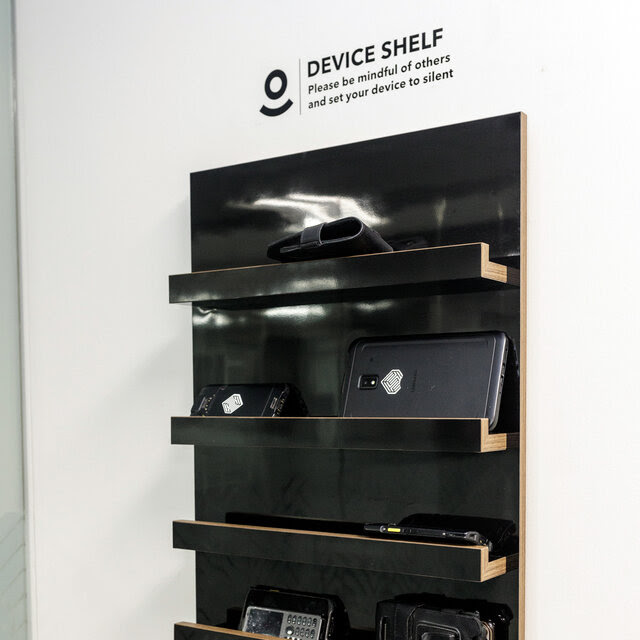 A black shelf holding various phones, attached to a white wall.