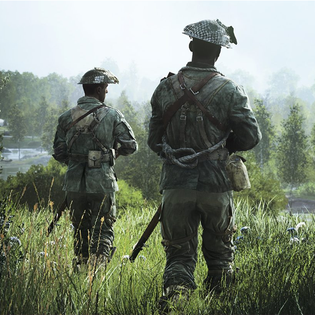 Two soldiers dressed in camouflage walk through grassy fields while carrying rifles.