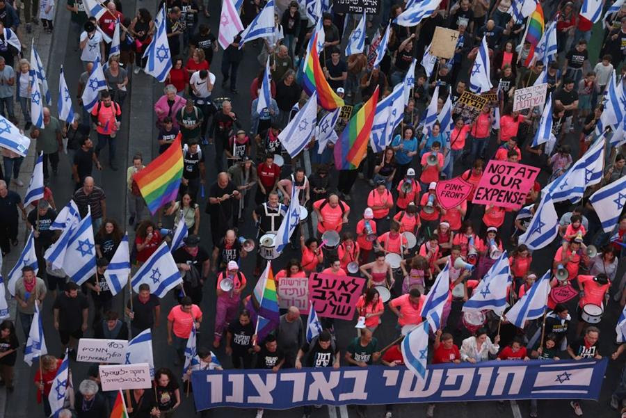 A scene of a protest, with Israeli flags and LGBTQ pride flags, viewed from above.