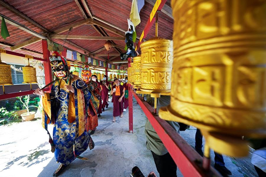 Monks wearing costumes and monks perform prayers in a Tibetan temple.