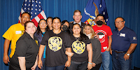 Secretary Walsh and Deputy Secretary Su pose with a group of immigrant workers and advocates. Some wear shirts with union logos. The American and Labor Department flags are visible in the background.  
