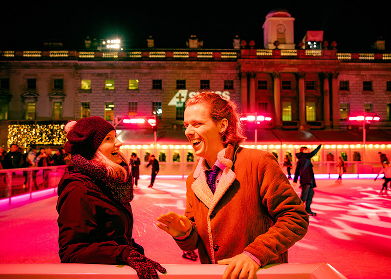 Two people are laughing together as they stand at the edge of the ice rink.