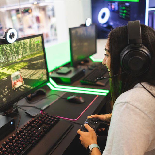 A woman sits happily playing a driving game on a PC using an Xbox One controller.