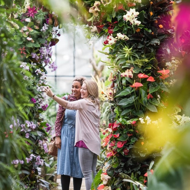 Two women take a selfie under a floral archway at Orchids.