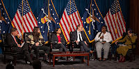 A six-person panel including Secretary Walsh and Rep. DeLauro sits on a stage in front of a backdrop of American and Labor Department flags.  