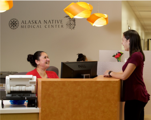 A woman talks to another woman sitting at a desk at the Alaska Native Medical Center.