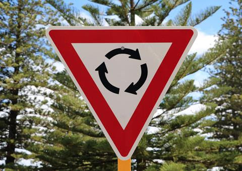 Photo of a roundabout sign - an upside down triangle with a red border and three arrows curving together to make a circle.
