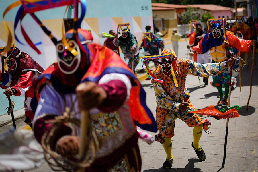 People dressed in colorful clothing and masks take part in a dancing devils procession.