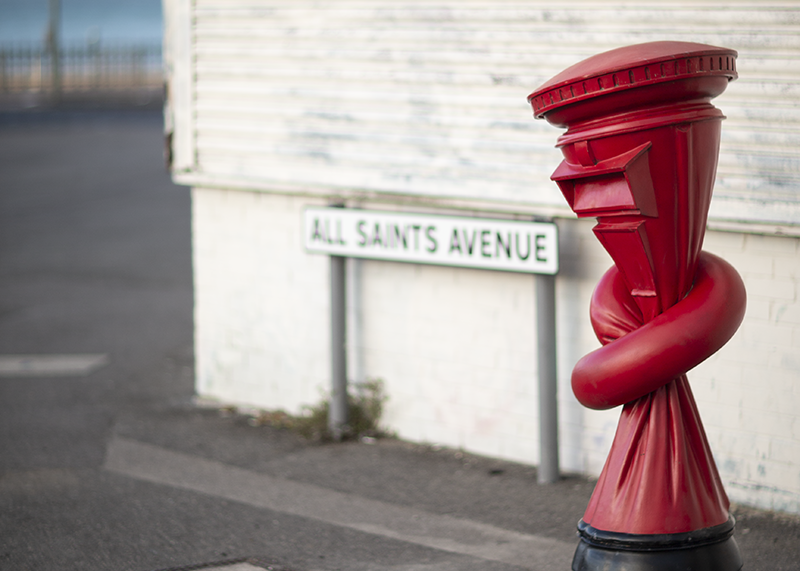 An artwork by Alex Chinneck. A sculpture of a red postbox is twisted in a knot.