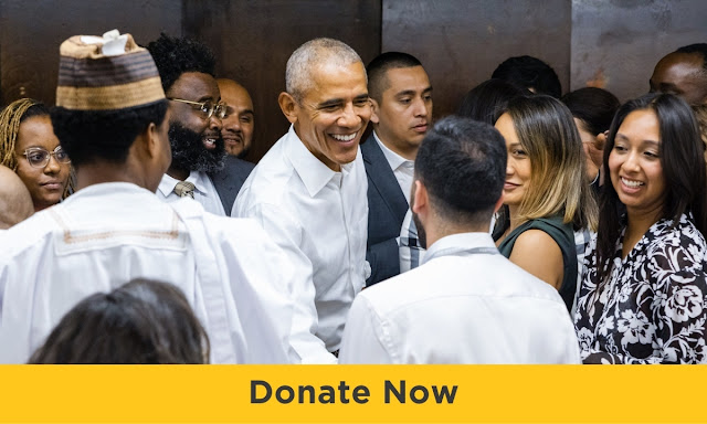 President Obama is shown wearing a white button up shirt and smiling amidst a group of people of varied skintones and hair types all dressed in business attire. On the bottom, a banner reads "Donate Now"