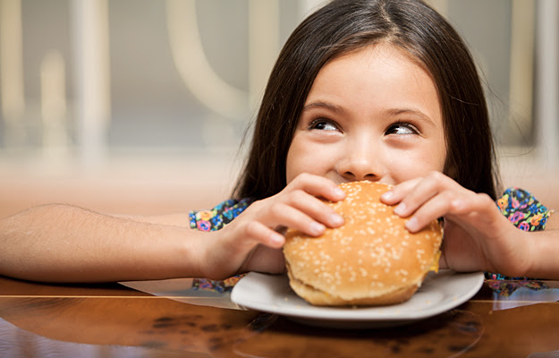 A young girl holding a cheeseburger with a sesame seed bun.