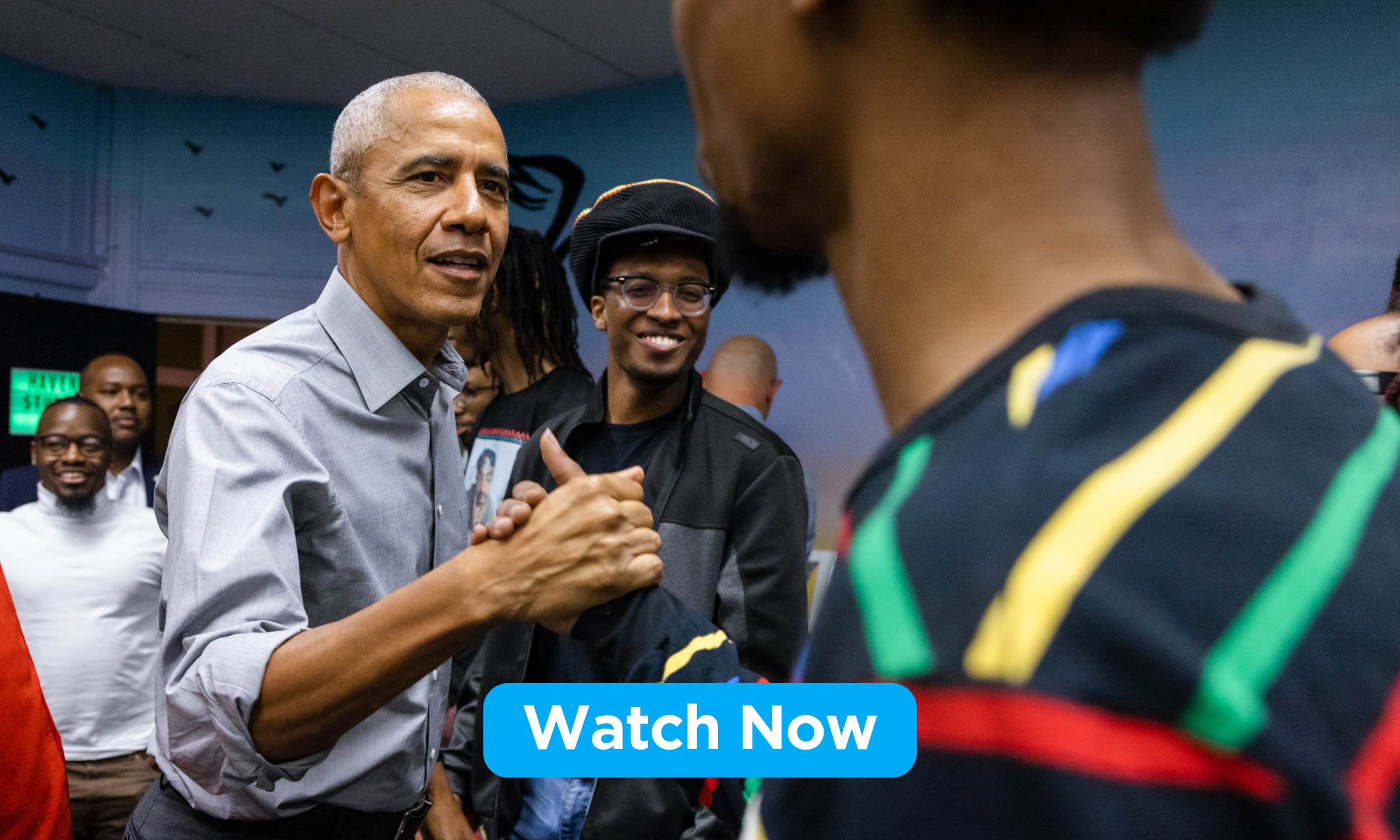 President Obama casually shakes hands with a young Black man with medium skin who wears a black shirt with colorful stripes. Other young men of medium-deep skin tones looks on and smiles.