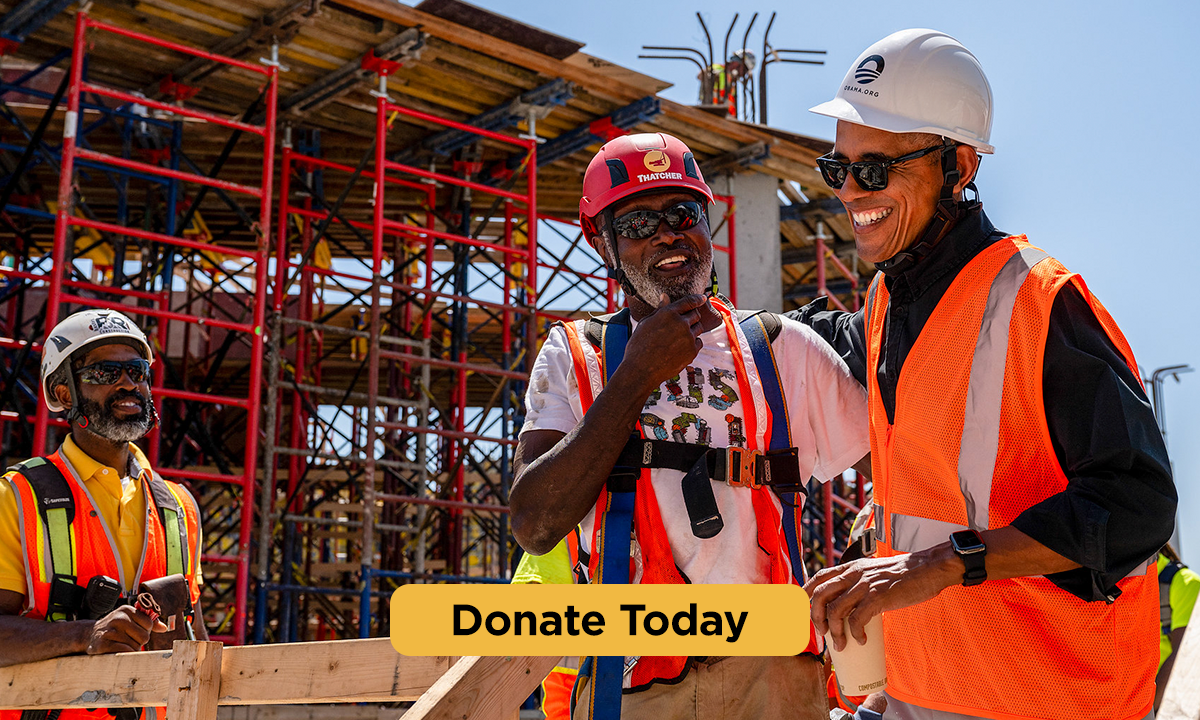 President Obama is wearing a hardhat and construction vest, laughing with a construction worker who has a dark skintone and is also wearing construction gear. In the background, another construction worker with a deep skintone and construction gear is looking on, surrounded by the scaffolding of a construction site. At the bottom, a button with the words "Donate Today"