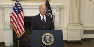 President Biden stands in front of a podium bearing the presidential seal at the White House.