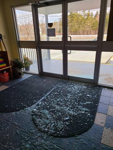 Photo of the smashed glass door of St. Luke's. Broken glass litters the floor.