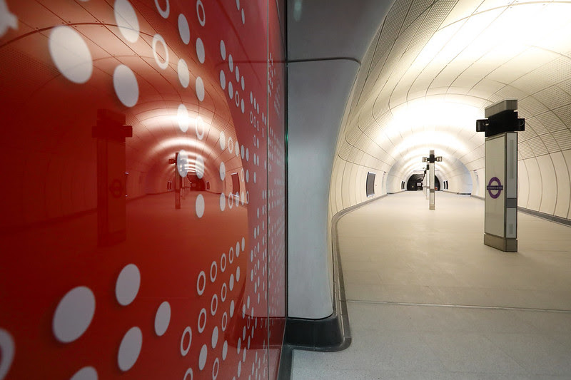 Tube station interior with a red wall with white spots and a curving white tunnel