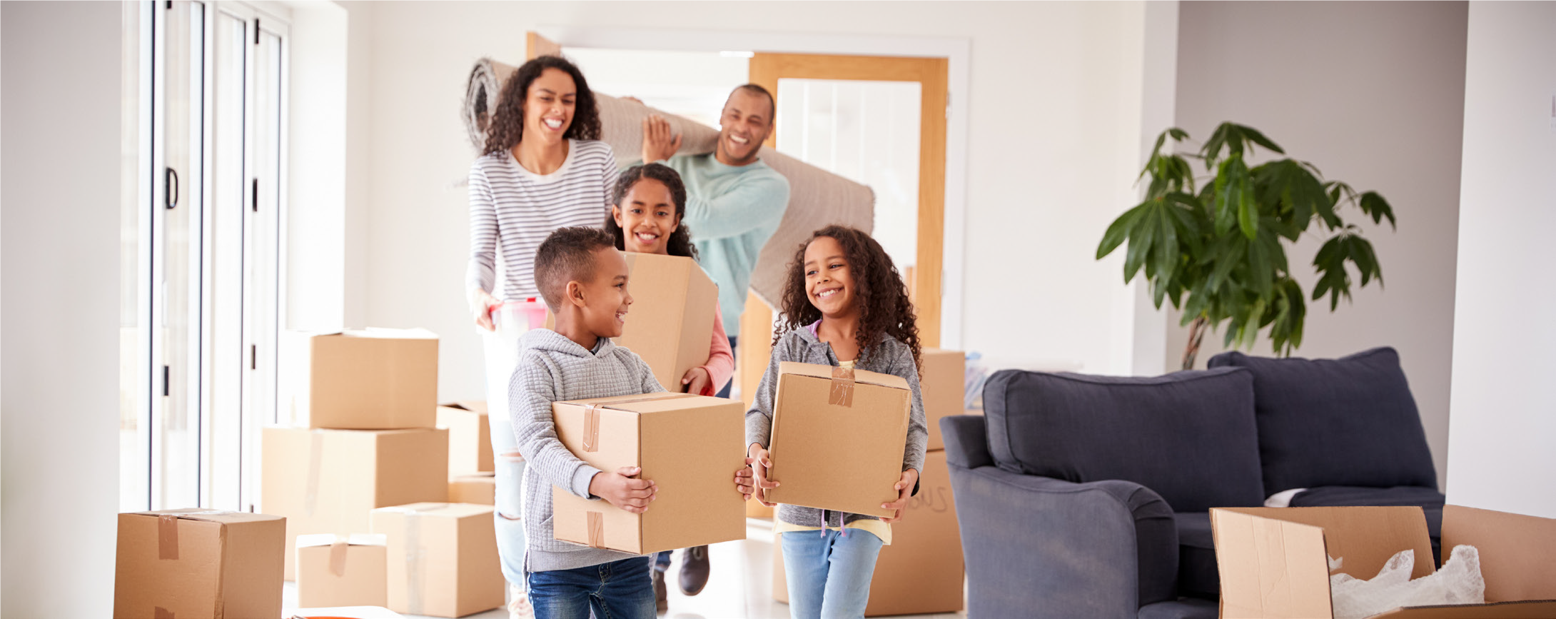 Photo of a laughing family (two adults, three children), surrounded by packing boxes in their new home.