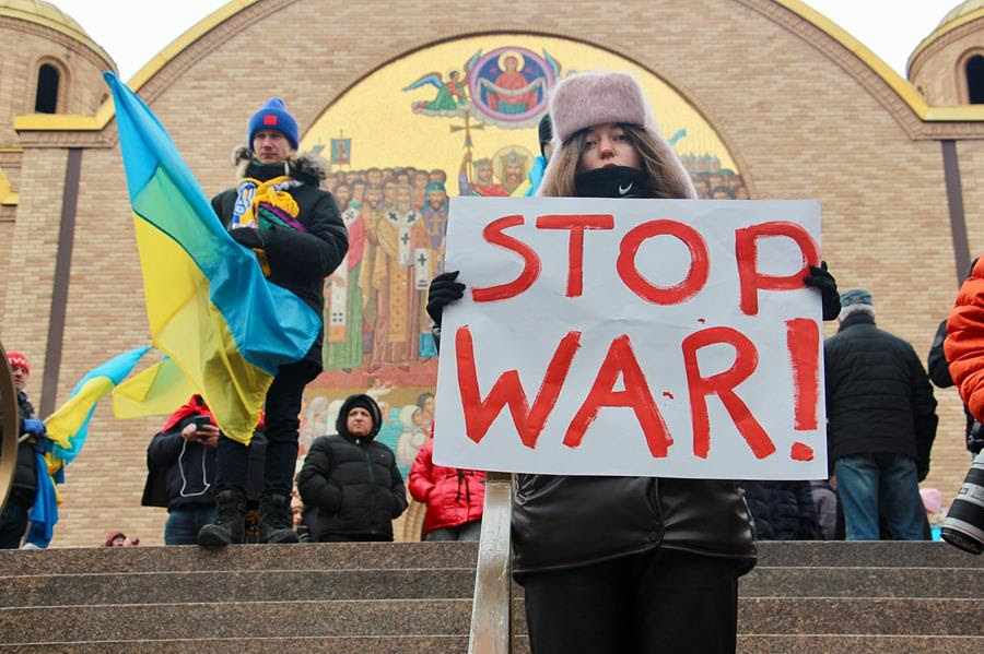 Inna Zotikova, 26, of Chicago, holds a sign during a rally outside the Sts. Volodymyr and Olha Ukrainian Catholic Church in Chicago's Ukrainian Village neighborhood. The sign says "STOP WAR!" in red. Behind her are other people. Several are holding Ukrainian flags.