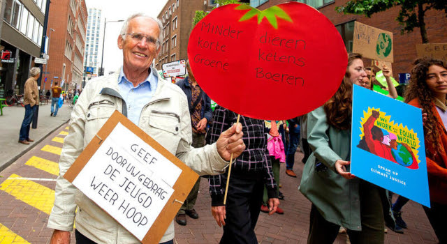 Een persoon tijdens de vorige klimaatmars die met borden aandacht vraagt voor  biologische landbouw en een oproep tot het geven van hoop aan de jeugd.