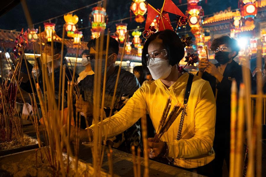 Worshippers at Wong Tai Sin Temple burn their first joss sticks of the new year. There are brightly lit lanterns overhead.