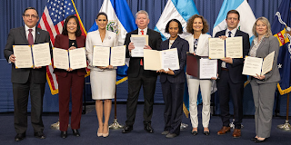 Deputy Secretary Julie Su poses with government representatives from El Salvador, Guatemala and Honduras in front of flags from all four countries. 