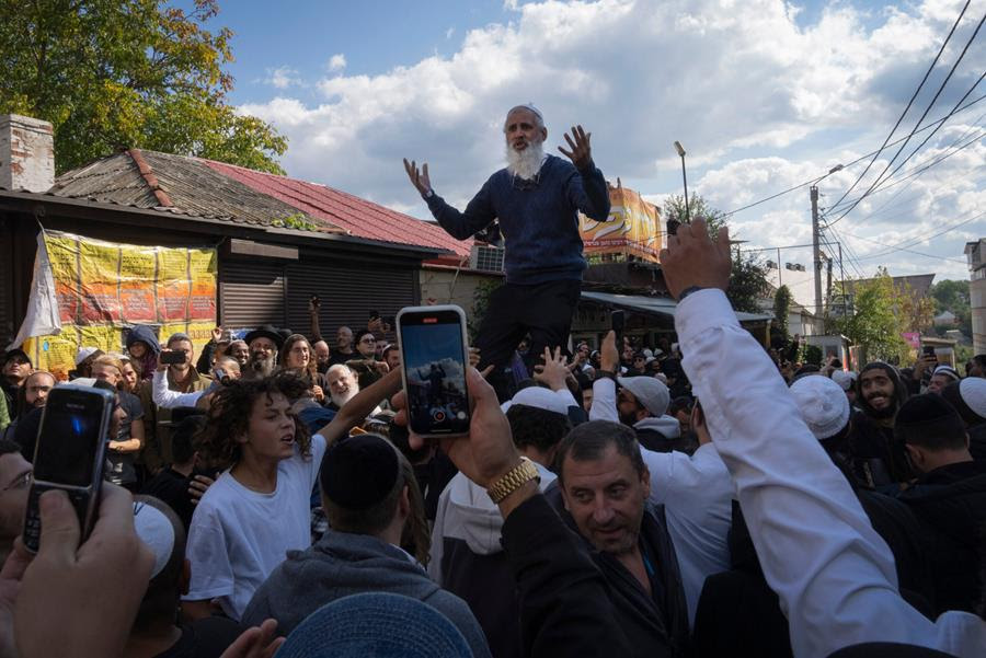 Orthodox Jews gather at the tomb of Rabbi Nachman, the great grandson of the founder of the Hasidic movement. There is one man who has been raised above the crowds and various people are holding their phones up to record him as he speaks.