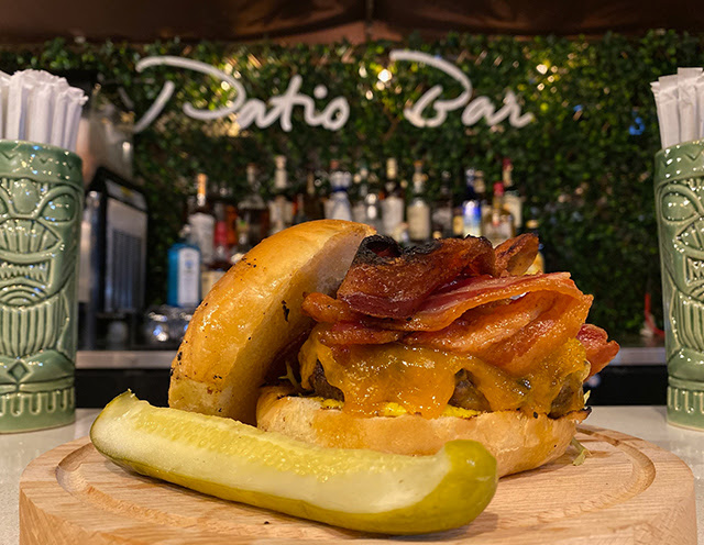 Close up of a bacon cheese burger with the Patio Bar sign in the background