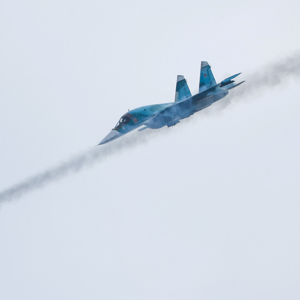 A blue fighter jet, its nose pointing down, flies through a gray sky, with two missiles in front.