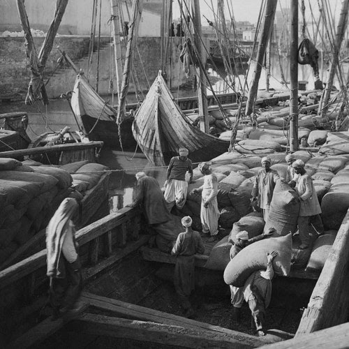 People load large sacks of cotton onto a boat.