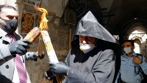 An Armenian priest wearing a protective mask and gloves passes on the Holy Fire lit in the church of the Holy Sepulchre