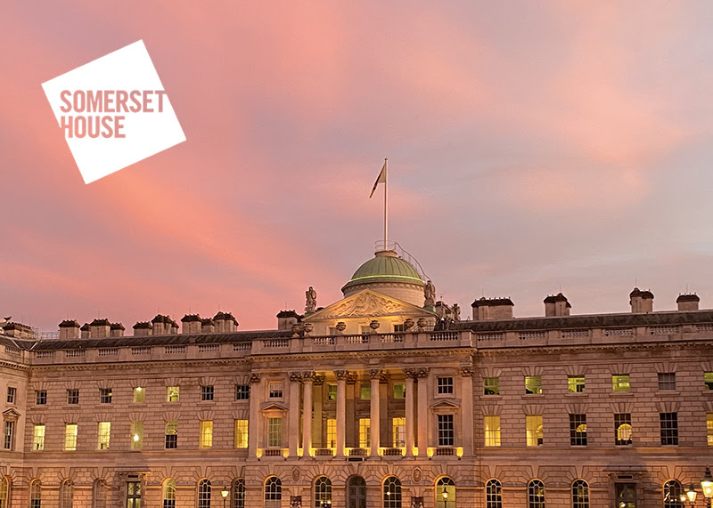 A photo by Takis Zontiros. It shows Somerset House at dusk. The south wing of the building has warm glowing lights from windows, and the sky is a lovely pastel pink and blue.